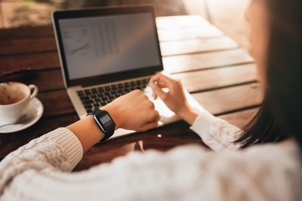 Woman looking at wrist watch while sitting in front of a notebook computer