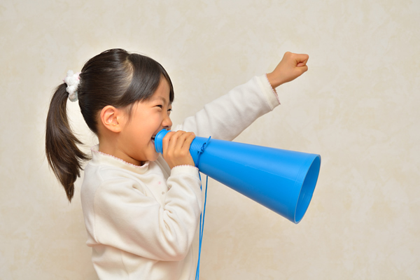 young girl with ponytail in white sweater talking through a blue megaphone